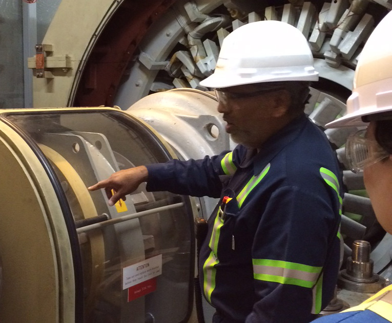 Employees in coveralls and hard hats examine equipment in a gas generating station.